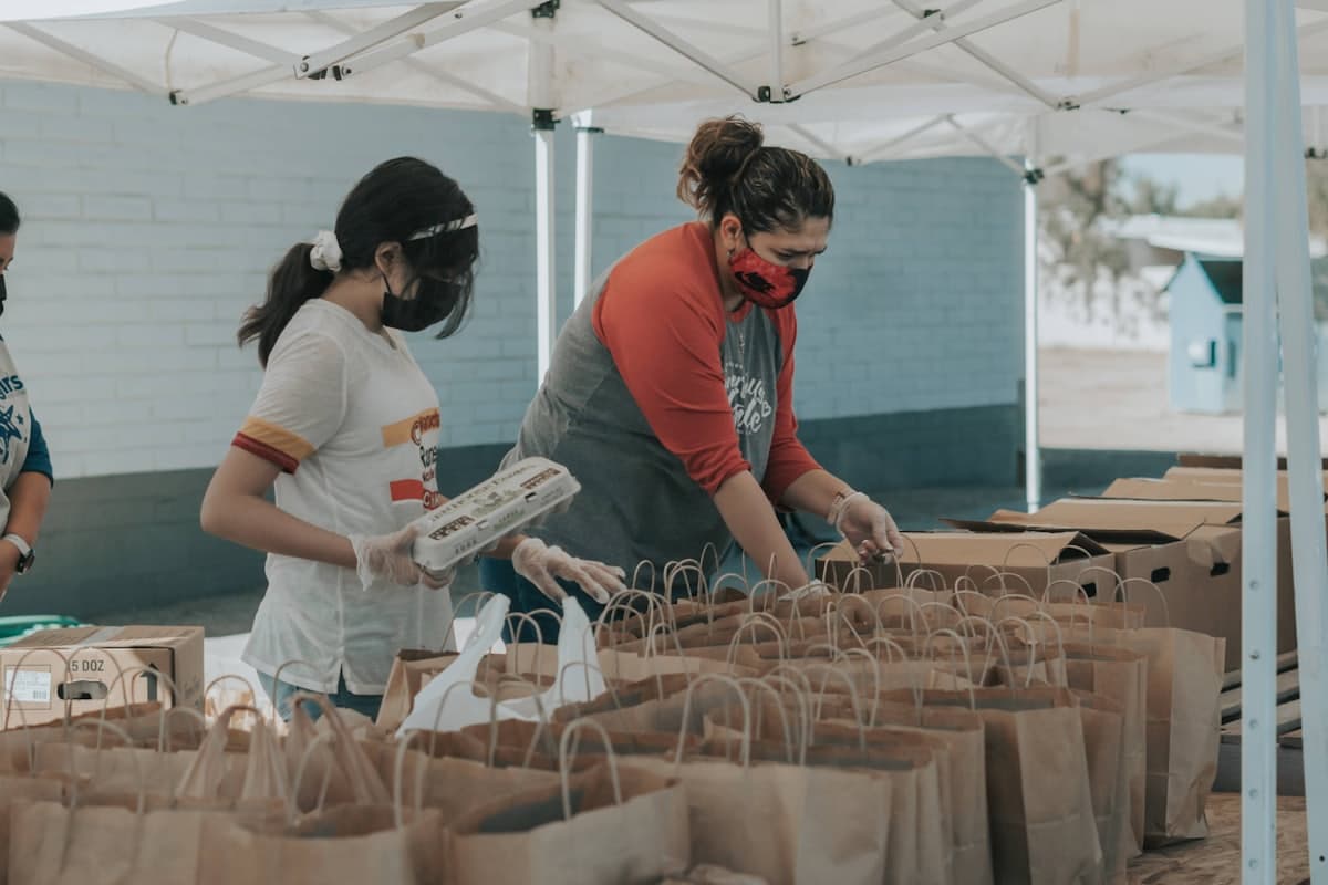 Volunteers packing paper grocery bags under a canopy at a community food distribution.